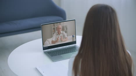 High-angle-view-of-video-conference-with-teacher-on-laptop-at-home.-Girl-in-video-call-with-personal-tutor-on-computer-listening-audio-course-distance-and-e-learning-education-concept.